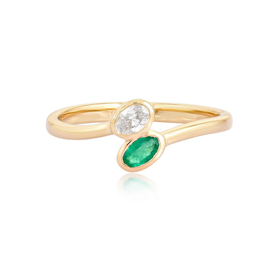 A gold ring featuring a marquise-cut green emerald and a round brilliant-cut clear diamond, set on a white background with a soft reflection.